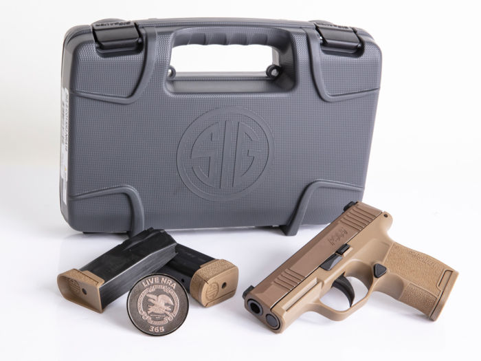 special edition NRA 9mm, striker-fired P365 micro-compact pistol with XRAY3 Day/Night sights, NRA branded P365 challenge coin, two (2) coyote tan 10-round flush fit magazines, and one (1) coyote tan 12-round extended magazine, placed in front of a hard shell pistol case with SIG logo.