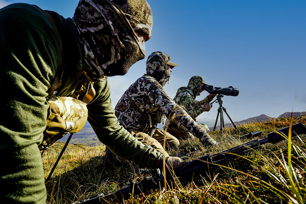  Two hunters in the field; one sights the range with a SIG SAUER rangefinder, while the other peers through the long range hunting scope mounted to the high power rifle.
