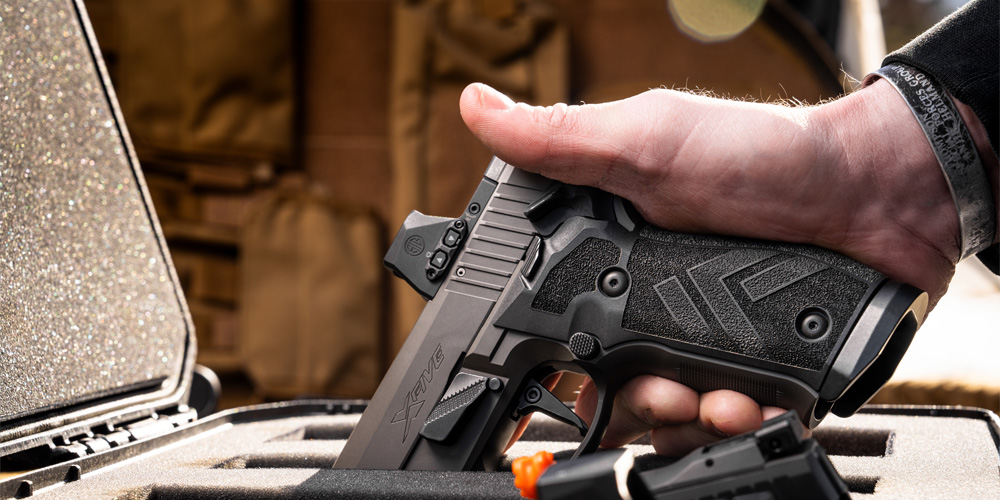 Man pulls his holstered pistol from his waist band holster in an off-road location with an off-road vehicle in the background.  